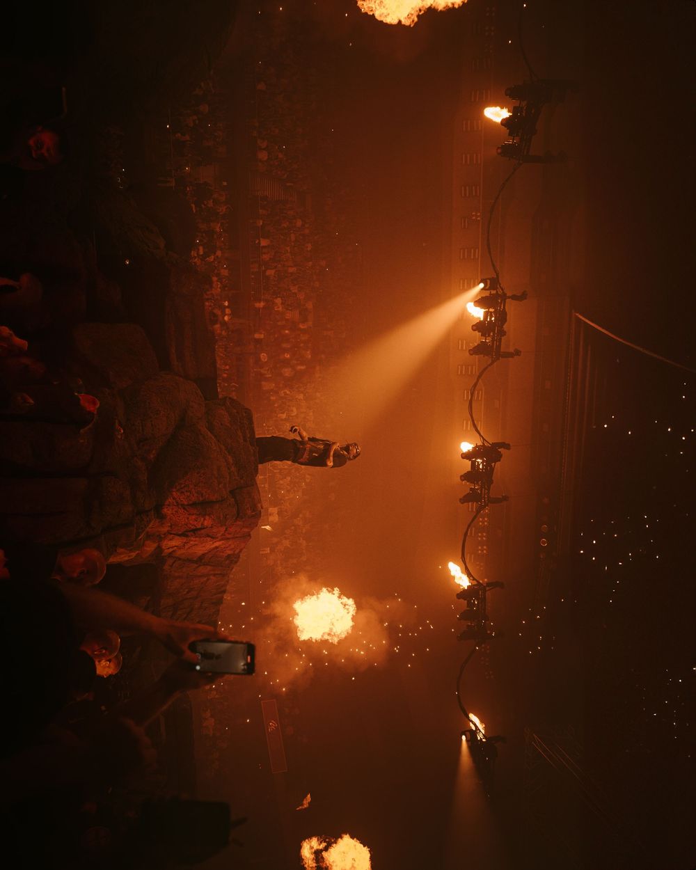 Dramatic orange stage lighting illuminates smoke and pyrotechnic effects during a theatrical performance.