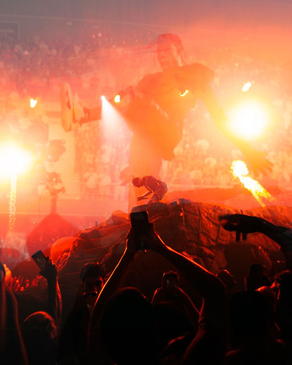 Silhouetted crowd at a sports event illuminated by bright orange flares and pyrotechnics creating a dramatic atmosphere.