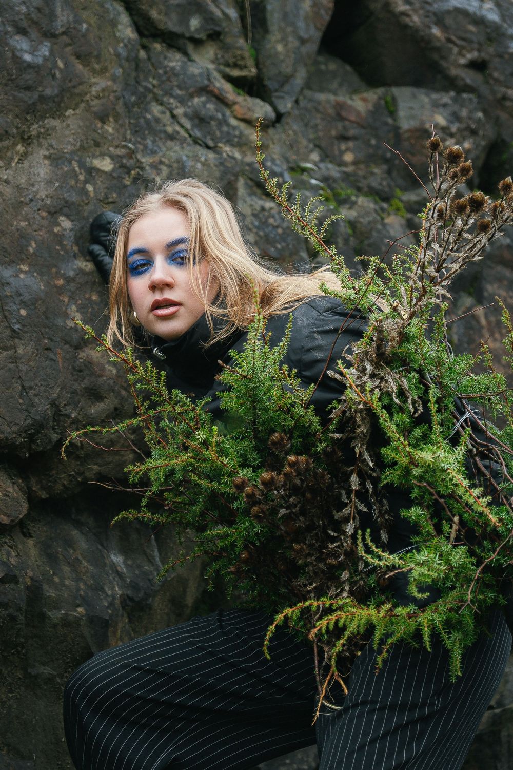 Artistic portrait series with greenery and dark rocky backdrop.