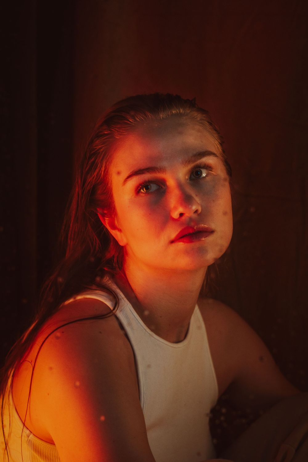 Dramatic close-up portraits in warm red lighting showing emotional expressions.