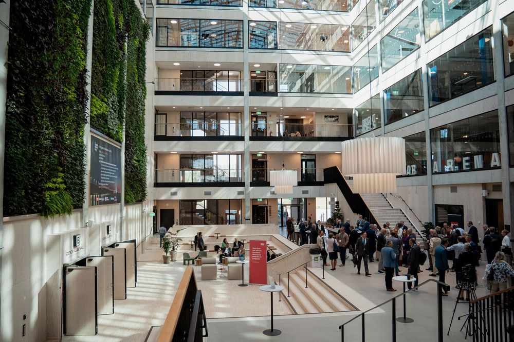 Modern office atrium with glass walls, escalators and indoor greenery.