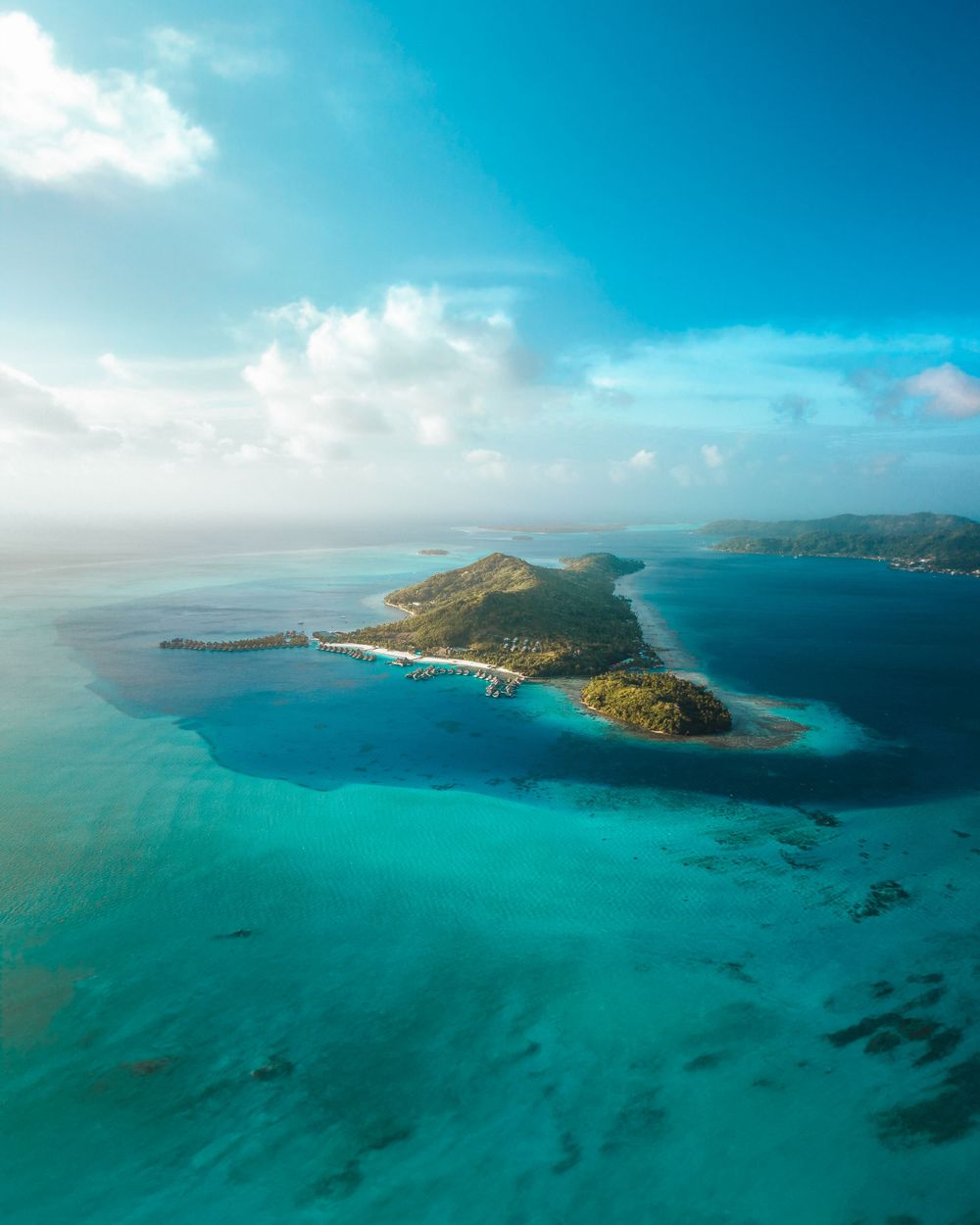 Aerial panoramic view of turquoise ocean waters surrounding mountainous islands with white sandy beaches and coastal cliffs.