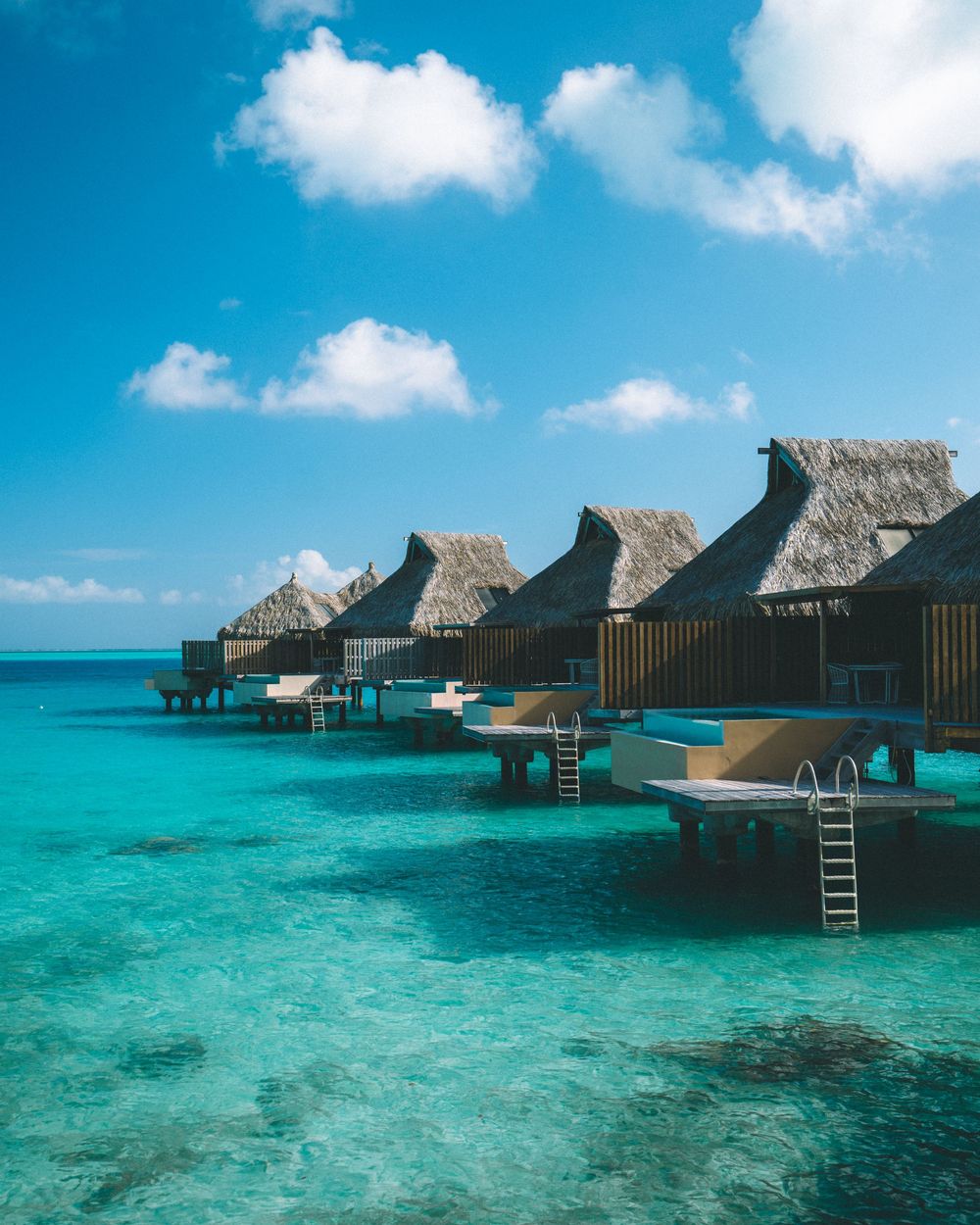 Luxurious overwater bungalows with thatched roofs line the crystal clear turquoise waters of a tropical paradise resort.
