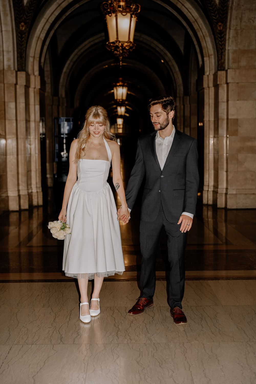 Couple walking together in a vintage interior hallway with arched ceilings and warm lighting.