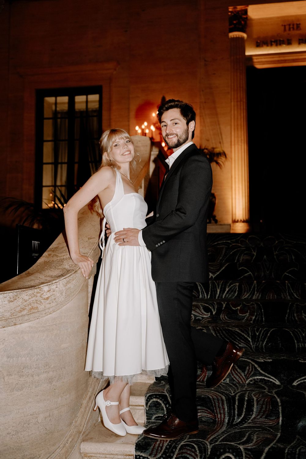A couple shares an intimate moment while dancing in an elegantly lit ballroom with chandelier lighting.