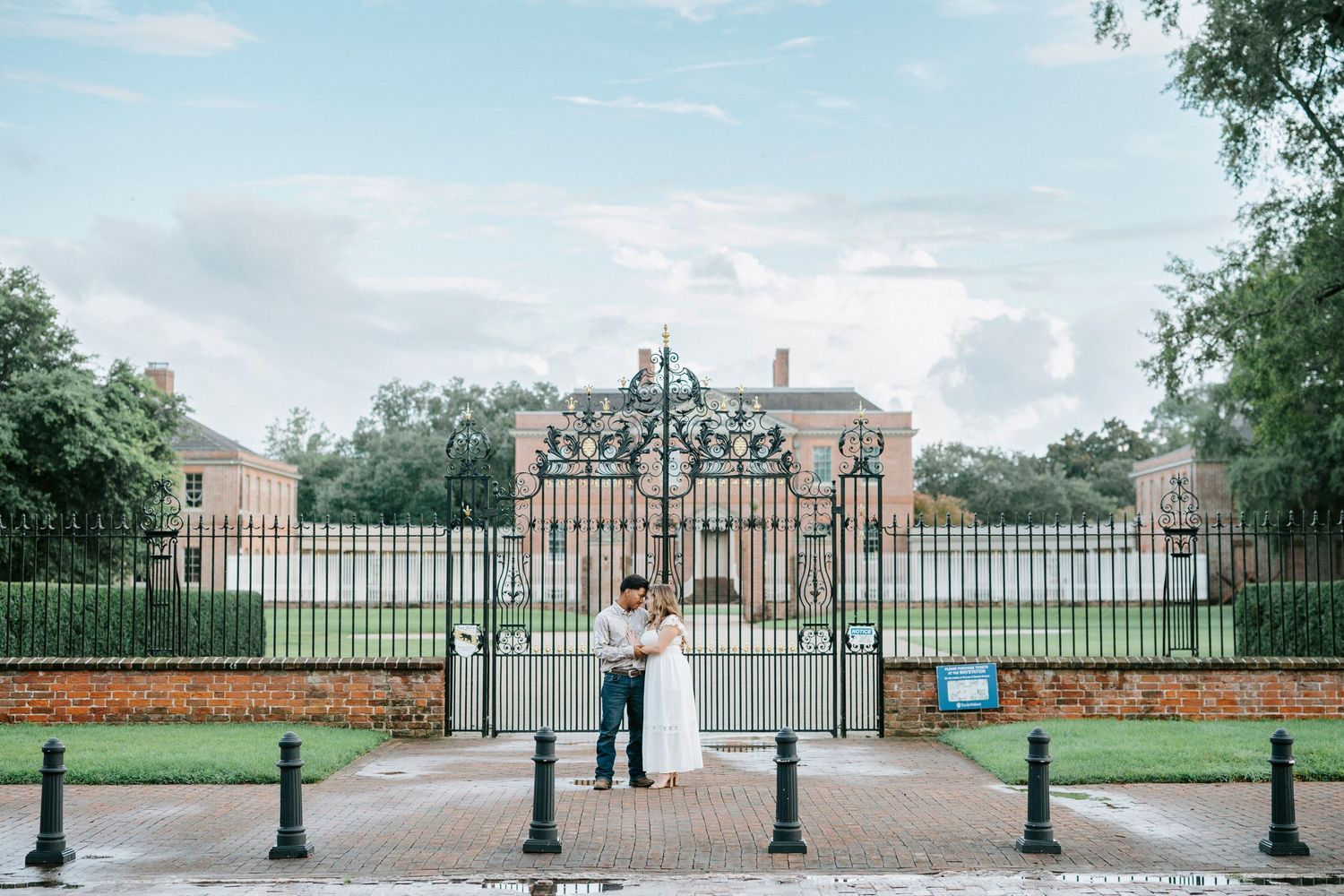 Panoramic view of an ornate black iron gate entrance with pillars leading to a grand estate or property.