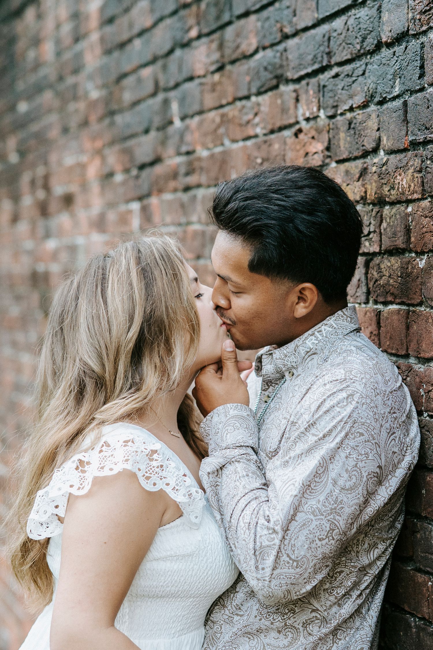 A romantic couple embraces against a rustic brick wall in an intimate moment.
