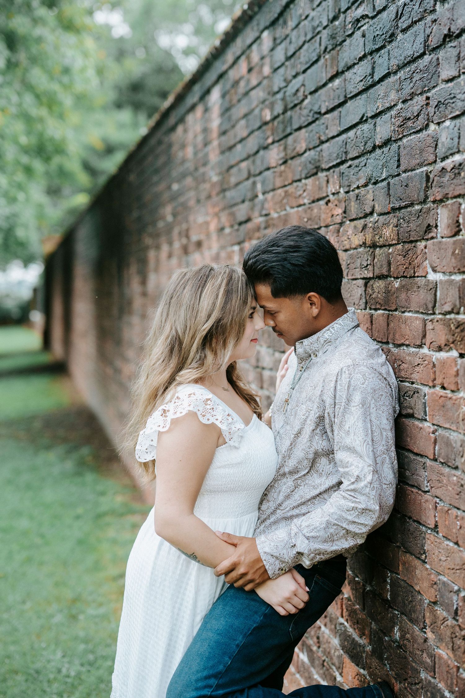 A romantic couple sharing tender moments against a rustic brick wall in a garden setting.