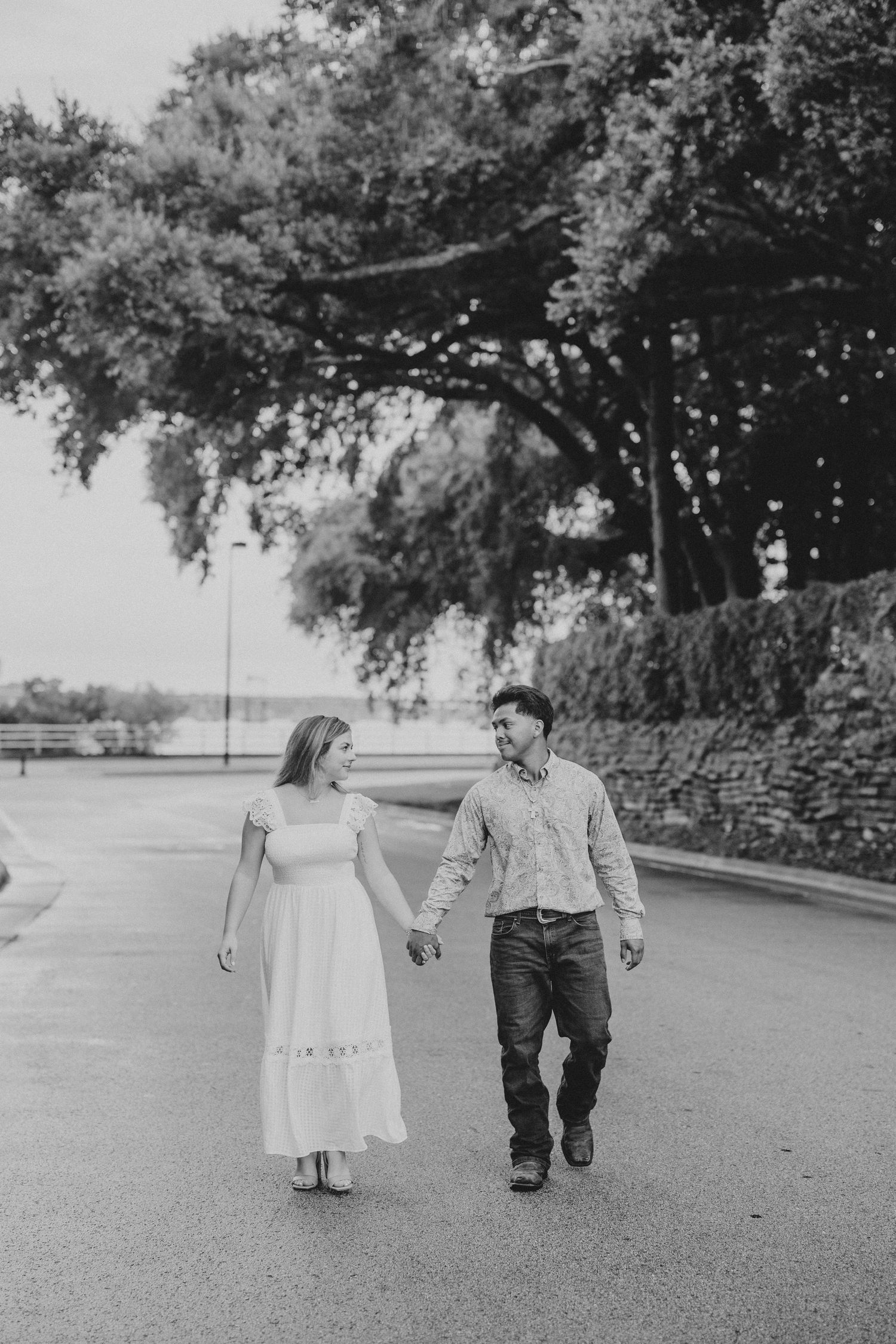 Two children walk hand in hand on a tree-lined path in a black and white photograph.