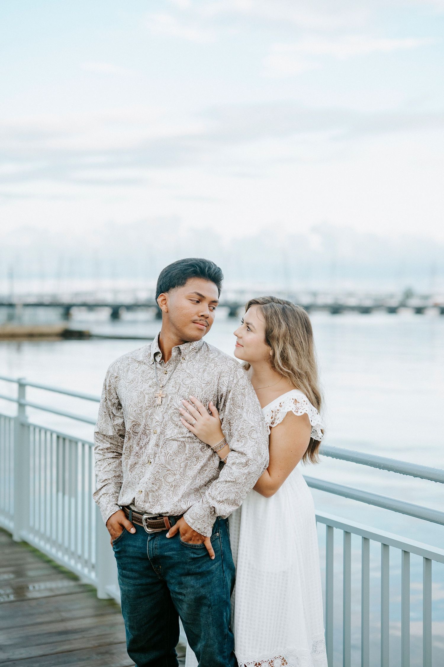 A romantic couple shares intimate moments while posing for photos on a boardwalk by the marina at sunset.