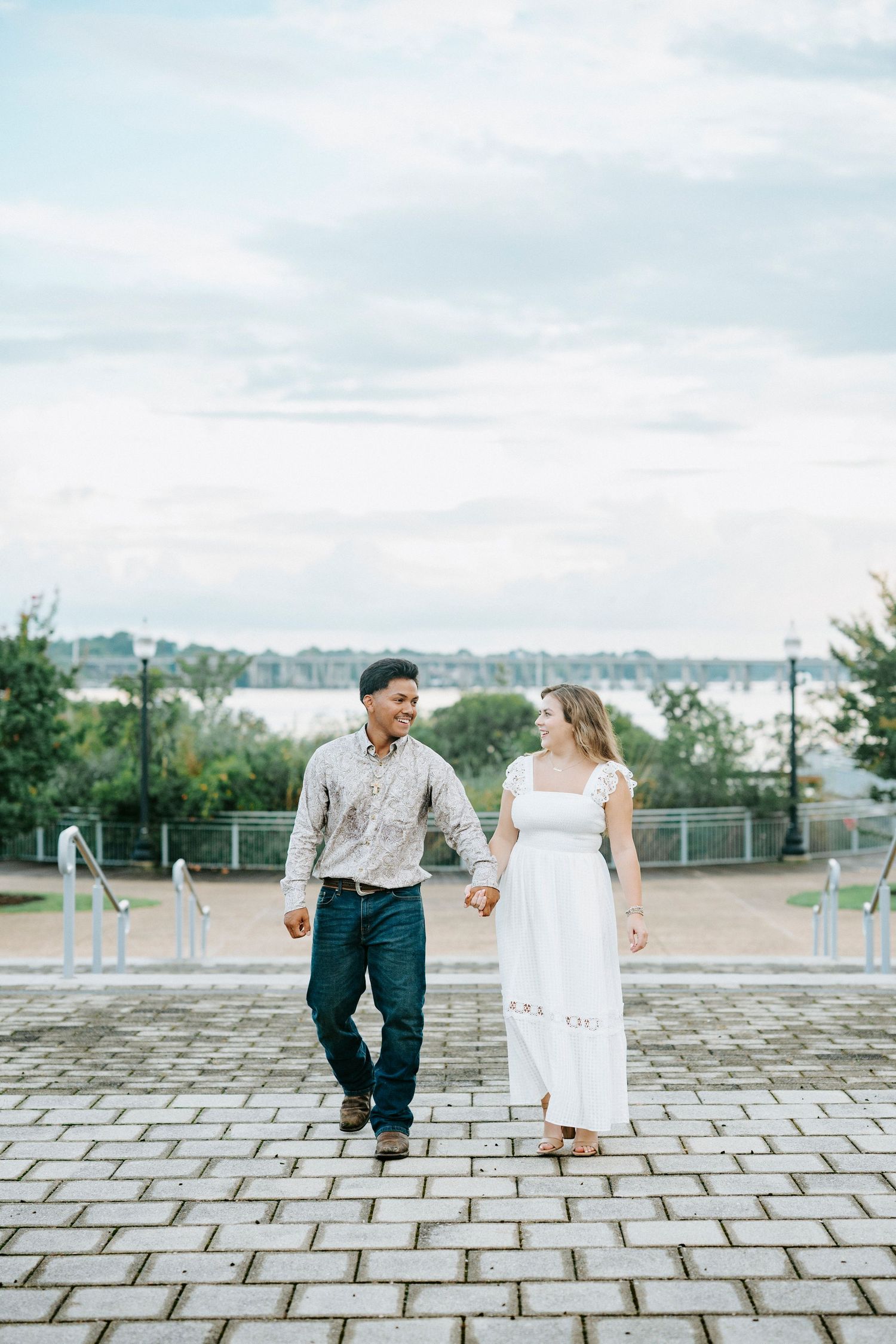 A couple dances and laughs together on a stone paved plaza with a cityscape backdrop.