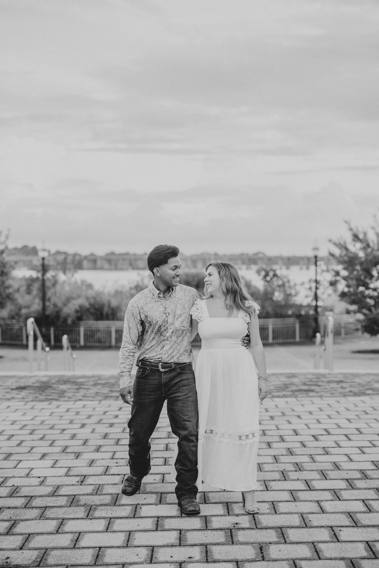 A couple shares intimate moments while posing together on a paved outdoor courtyard.