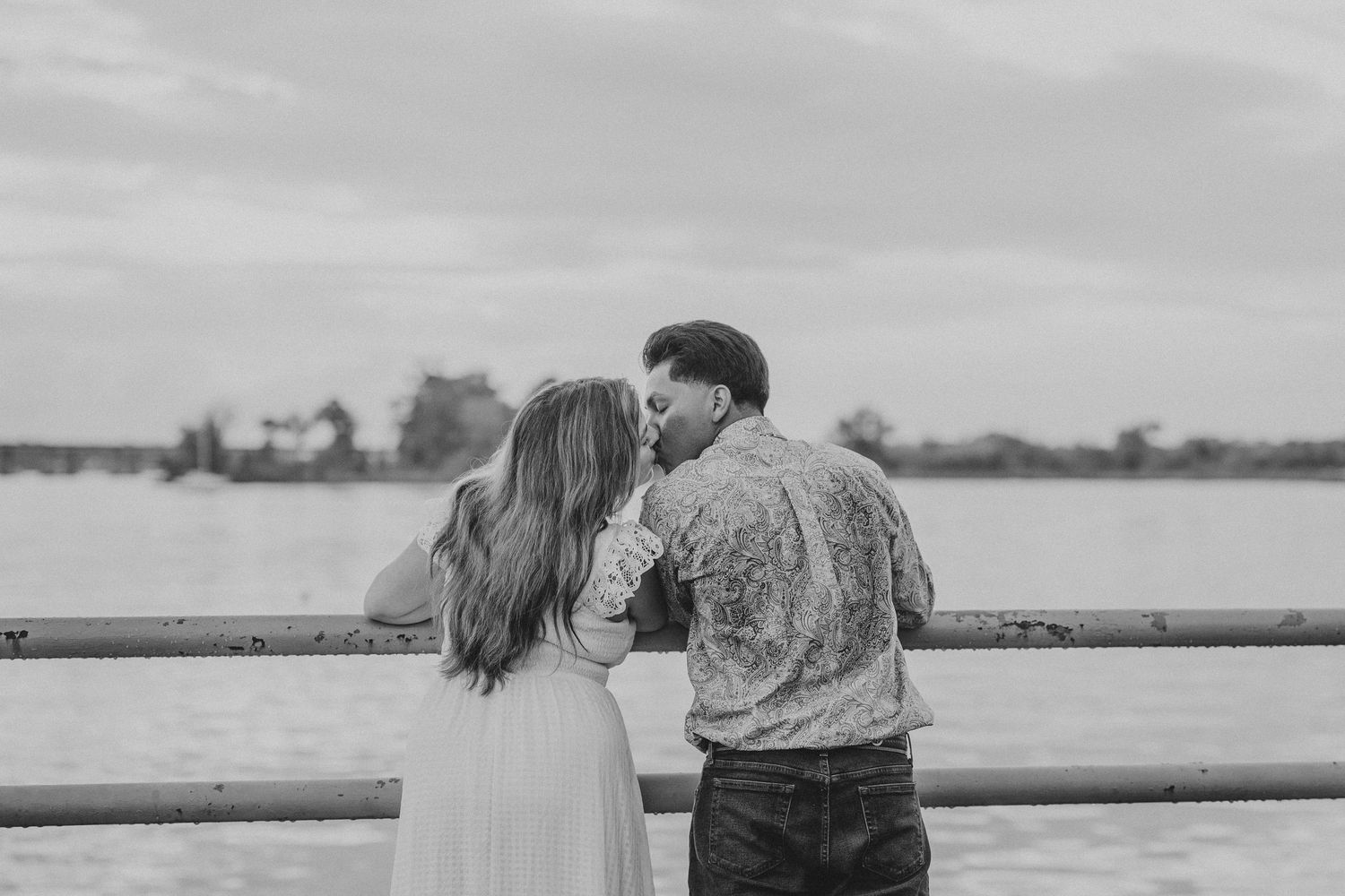 A couple enjoying a romantic moment on a wooden boardwalk overlooking the water at sunset.