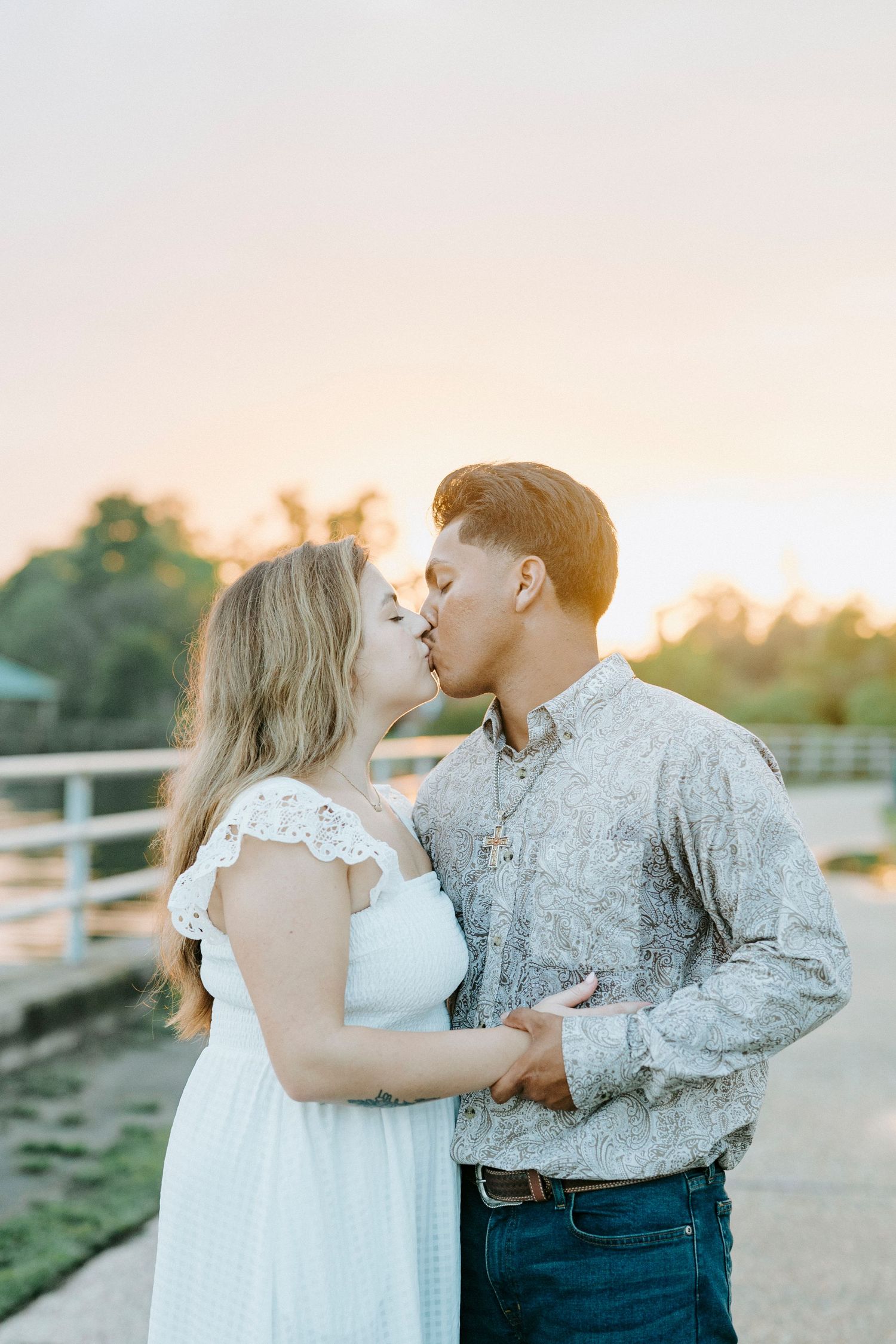 Couple sharing romantic moments at sunset by a wooden fence in a rustic outdoor setting.