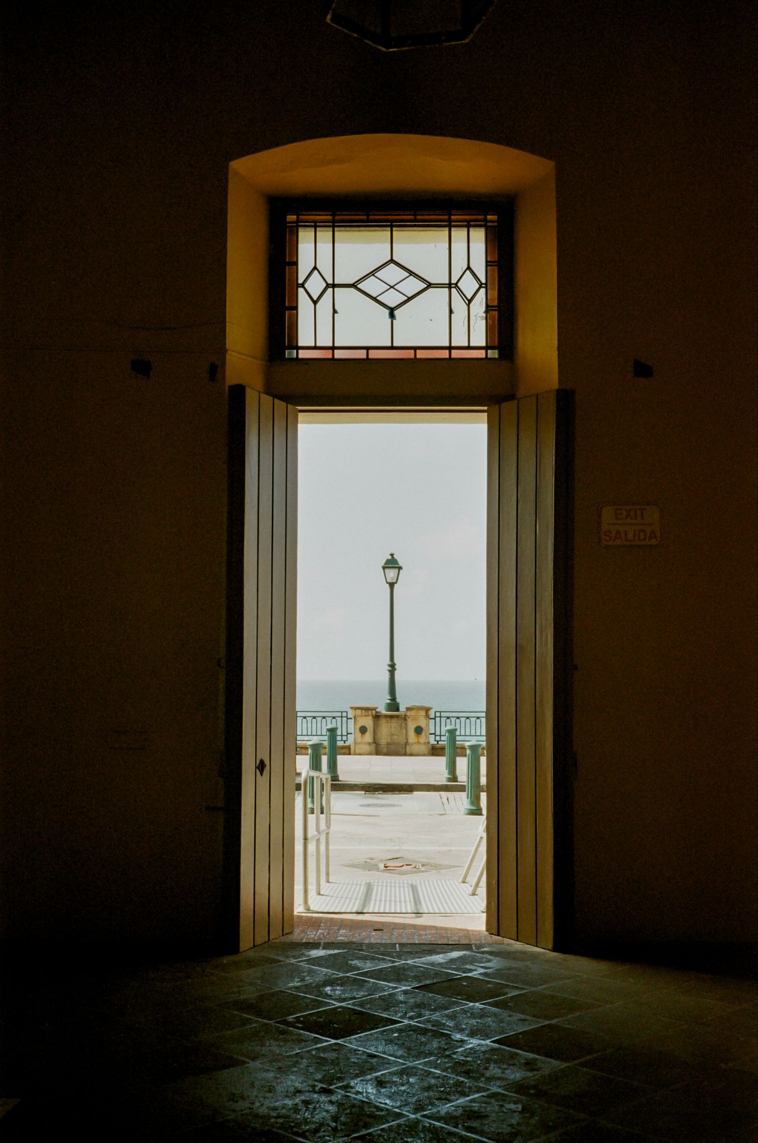 Looking through doorways of an abandoned building towards a lighthouse on a coast during sunset creates moody atmospheric scene.