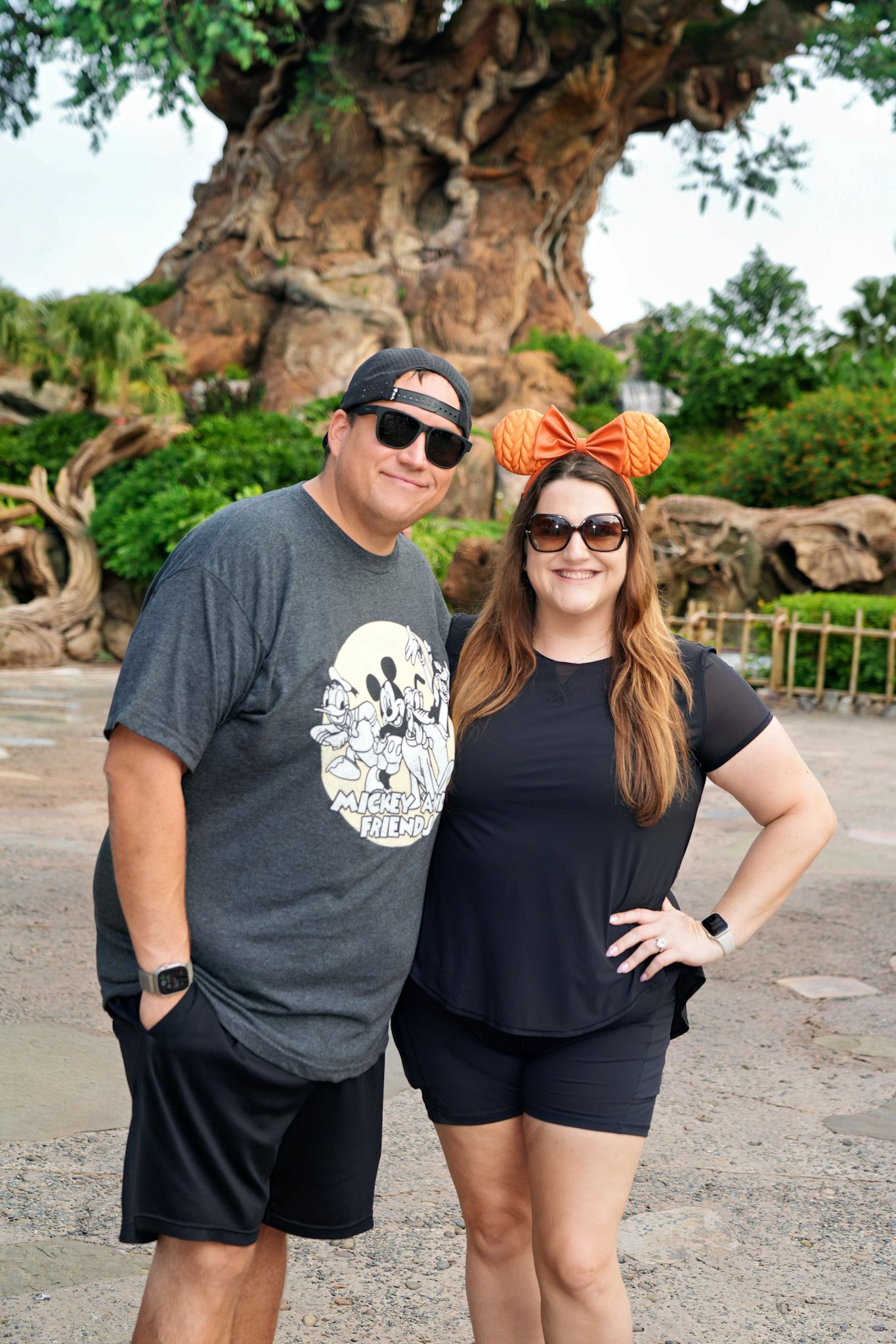 A couple wearing matching dark t-shirts pose together in front of a theme park setting.