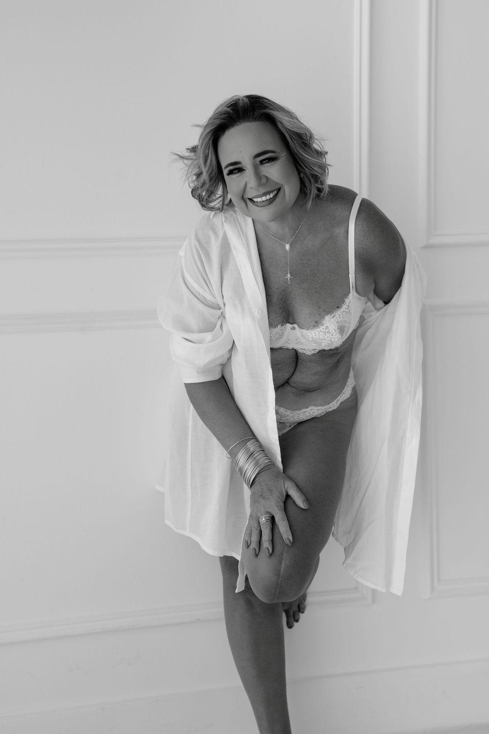 Natural light boudoir photography session capturing joyful poses in white decor.
