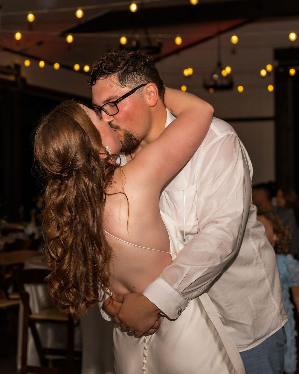 husband and wife kissing under the twinkling lights in the Chatfield farms barn