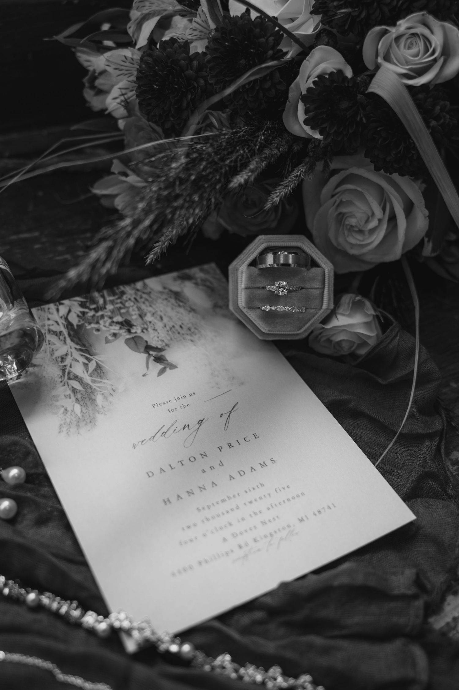 Black and white flat lay of wedding invitation for Dalton Price and Hannah Adams with rings and florals.