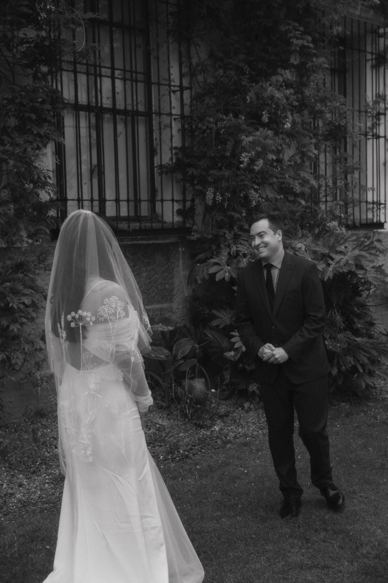 A black and white photo of a wedding scene in a garden with a bride in white dress and veil facing another person.