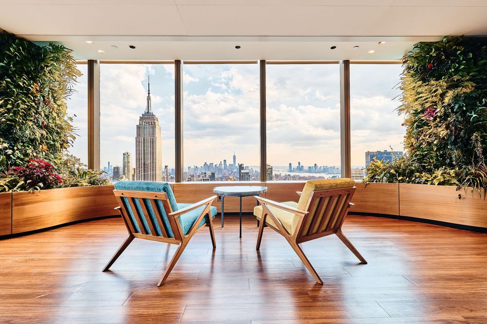 Modern lounge chairs face floor-to-ceiling windows with stunning Manhattan skyline views in a luxury penthouse space.