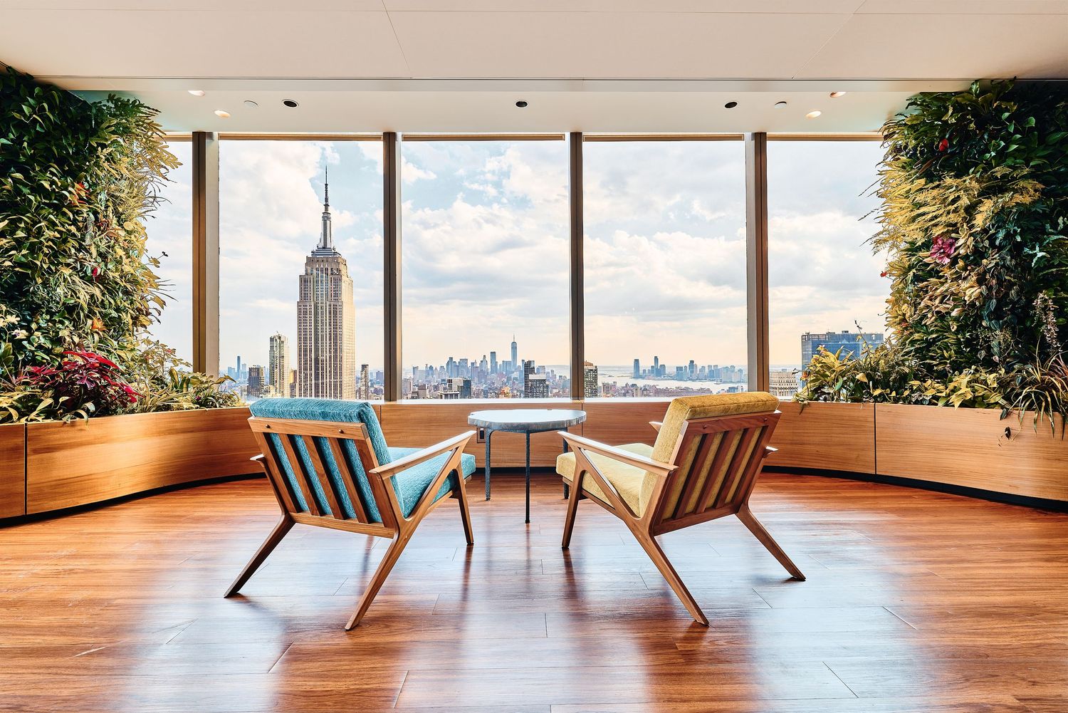 Modern lounge chairs face floor-to-ceiling windows with stunning Manhattan skyline views in a luxury penthouse space.
