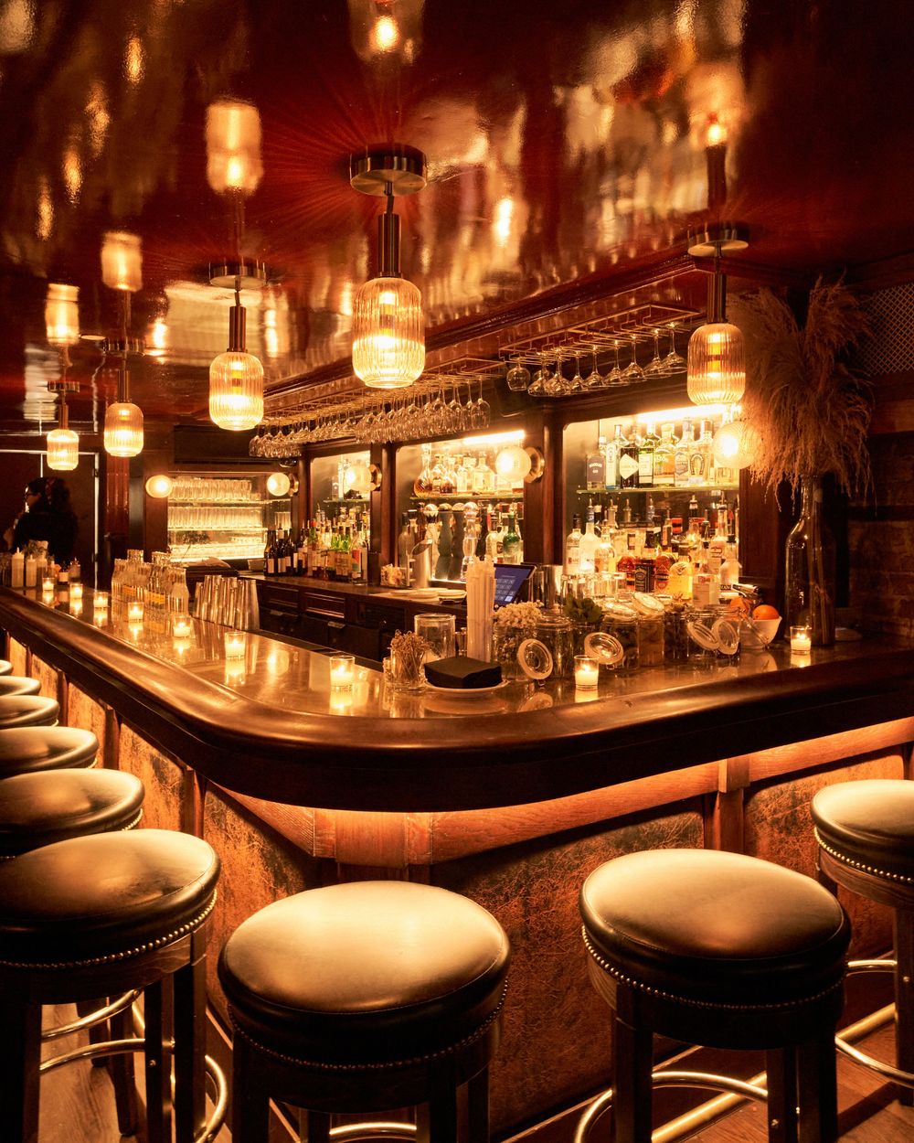 Dimly lit upscale cocktail bar interior with warm glowing pendant lights and curved leather banquettes creating an intimate atmosphere.