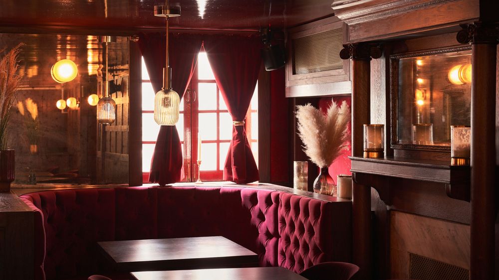 Panoramic view of an elegant restaurant interior with red leather booths, wooden tables, and warm pendant lighting.