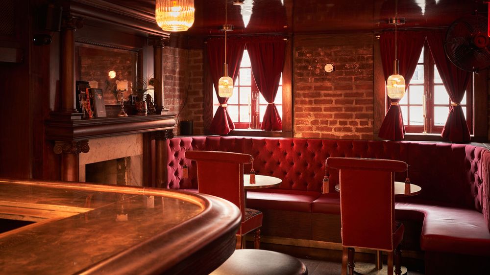 Cozy bar seating area with red leather banquettes and exposed brick walls illuminated by warm pendant lights.