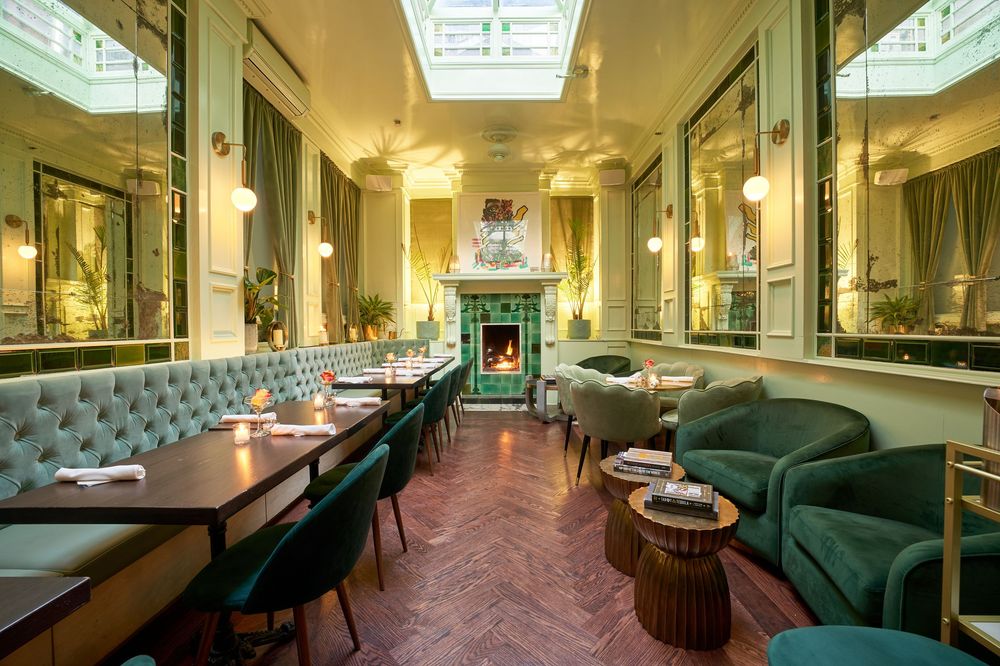 Elegant restaurant interior with tufted green velvet booths, mirrored walls, and modern pendant lighting creates luxurious ambiance.