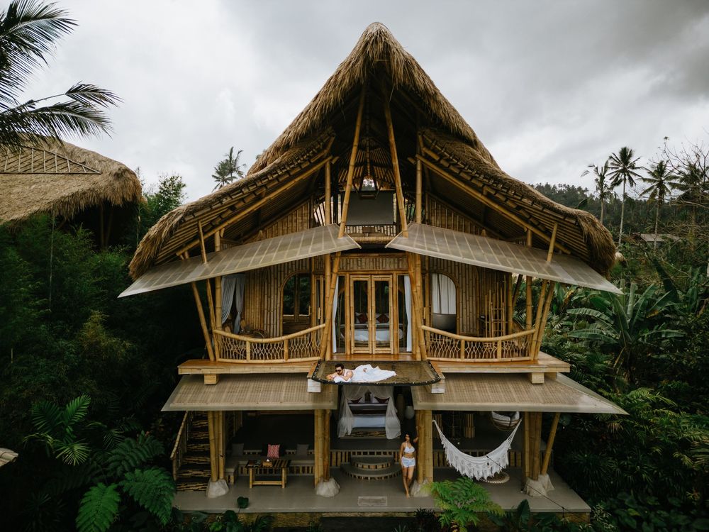 Modern bamboo treehouse with multiple levels and balconies surrounded by palm trees.