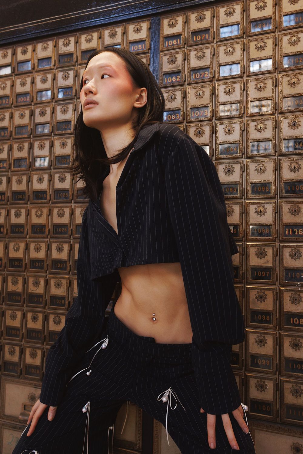 Fashion model in black attire poses dramatically against vintage wooden post office boxes in artistic portrait series.
