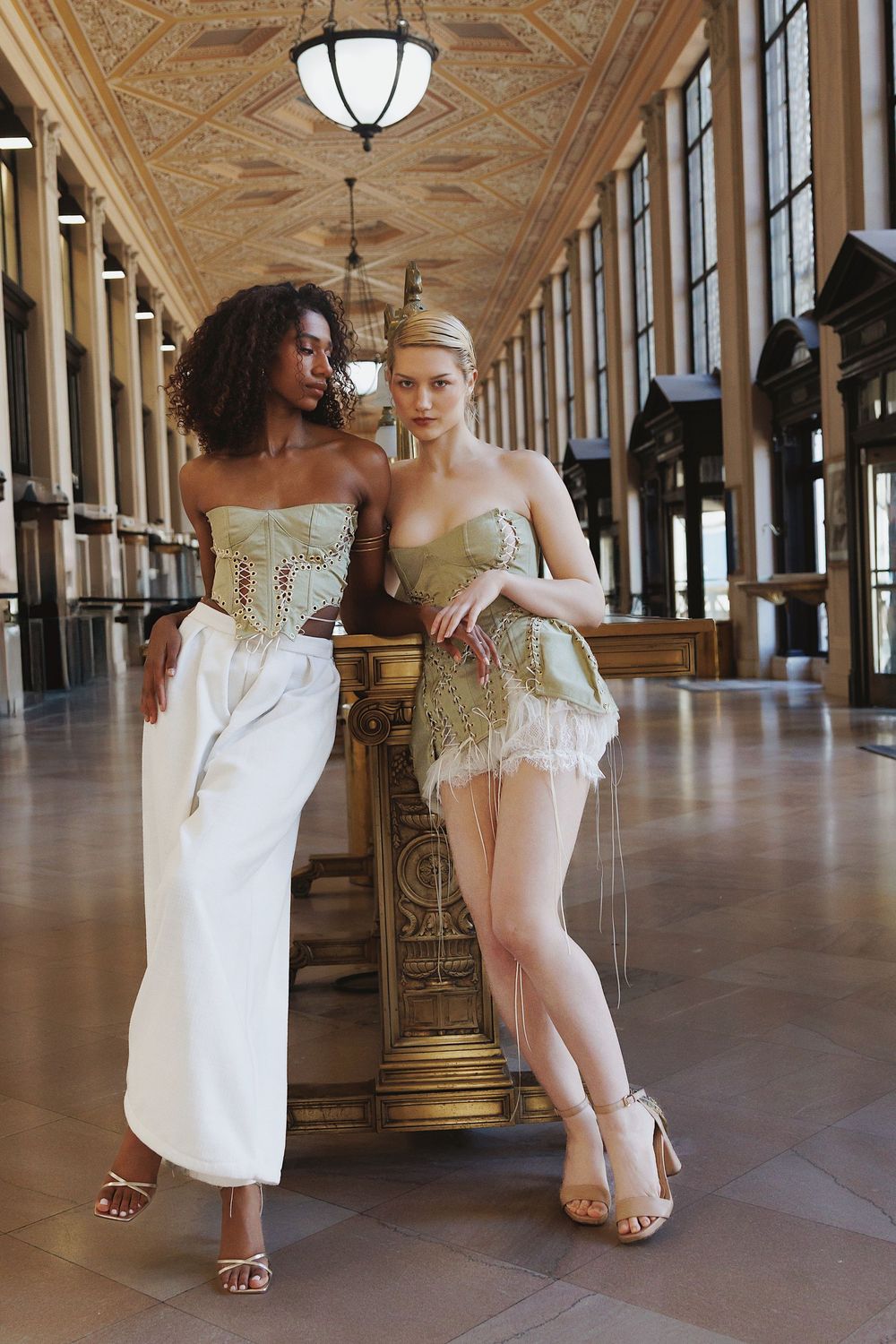 Ballet dancers in white costumes perform gracefully in an ornate classical corridor with decorative ceiling and lighting.