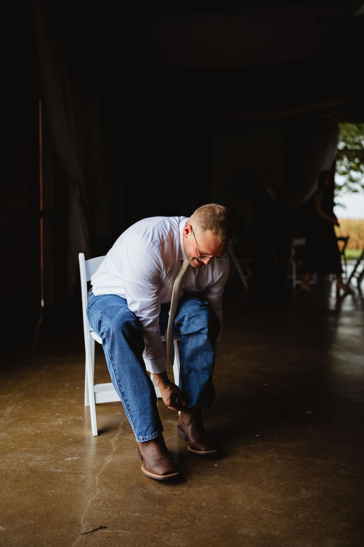 A person in a white shirt and jeans kneels down in a dimly lit interior space.