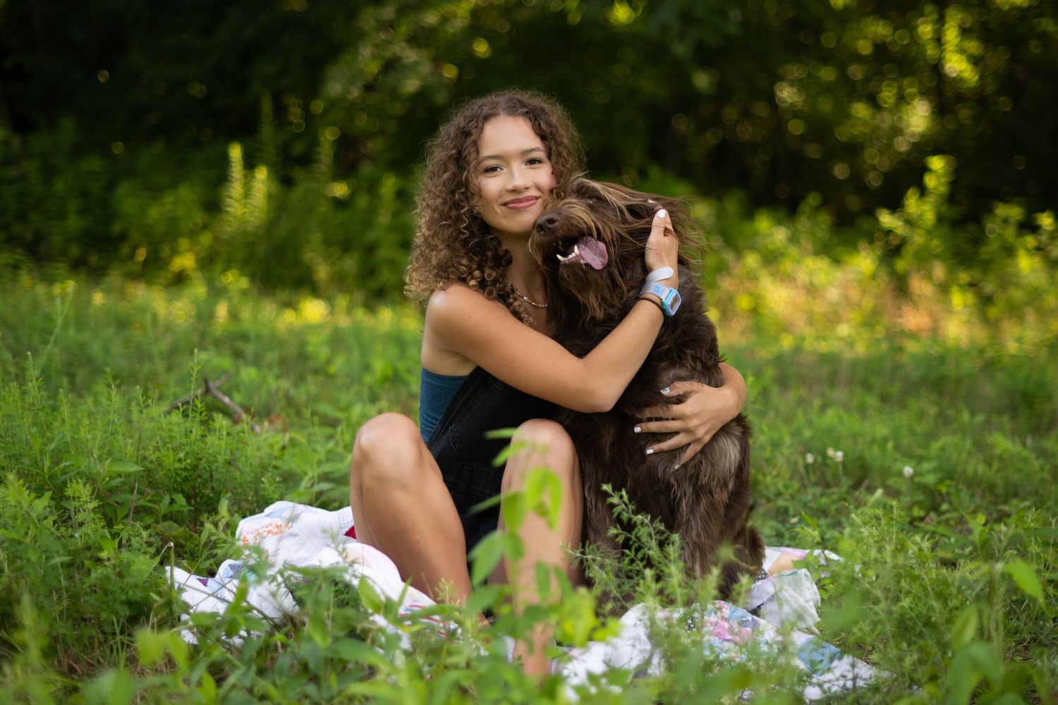 Person cuddling adorable brown dog outdoors in green grass field with white flowers on sunny summer day.