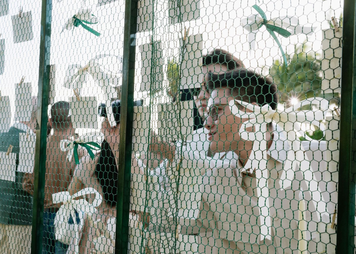 Wedding guests interacting through a decorative wire mesh panel adorned with green and white ribbon accents.