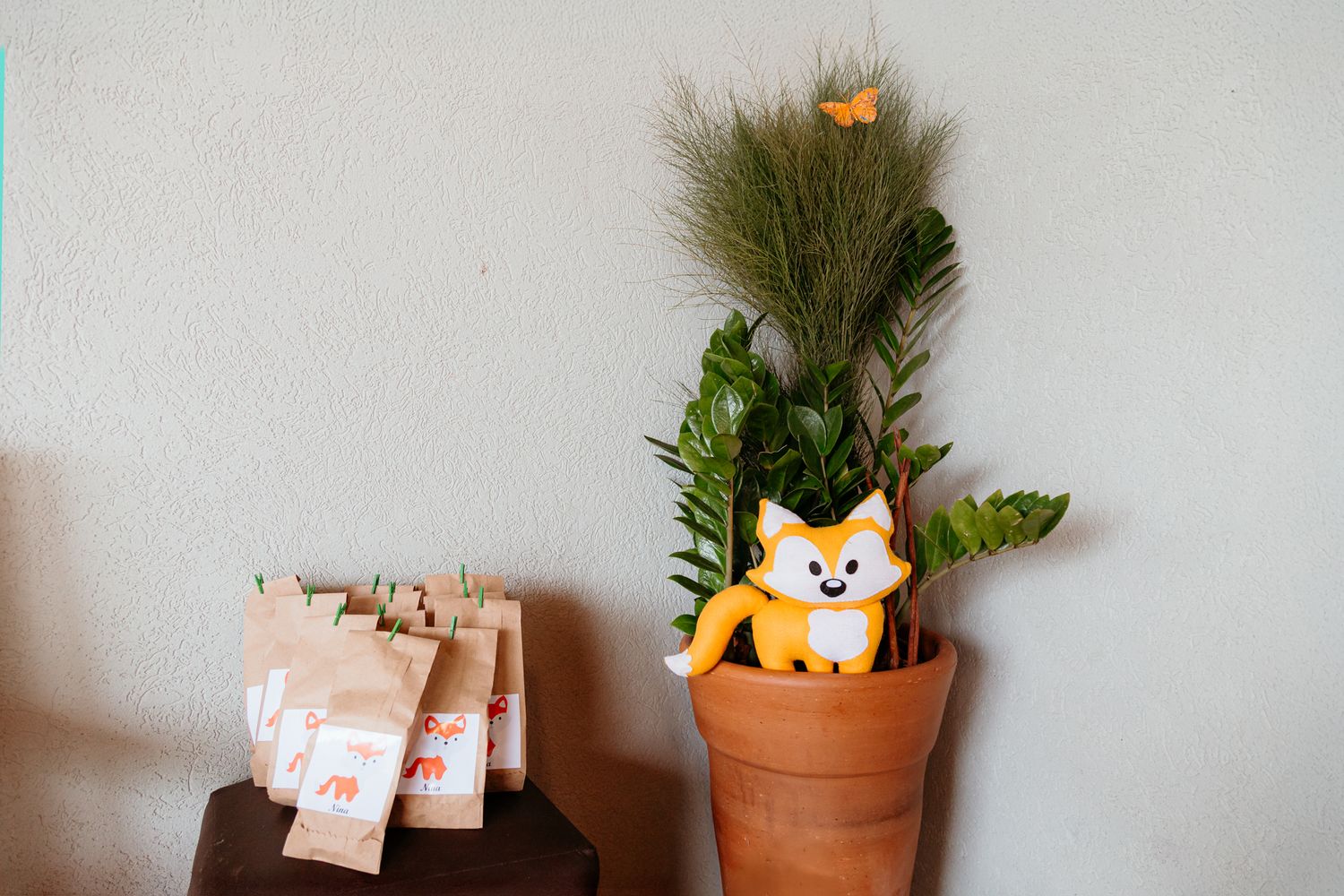 Decorative fox plush peeking out of terracotta pot with greenery and dried flowers beside paper tags.