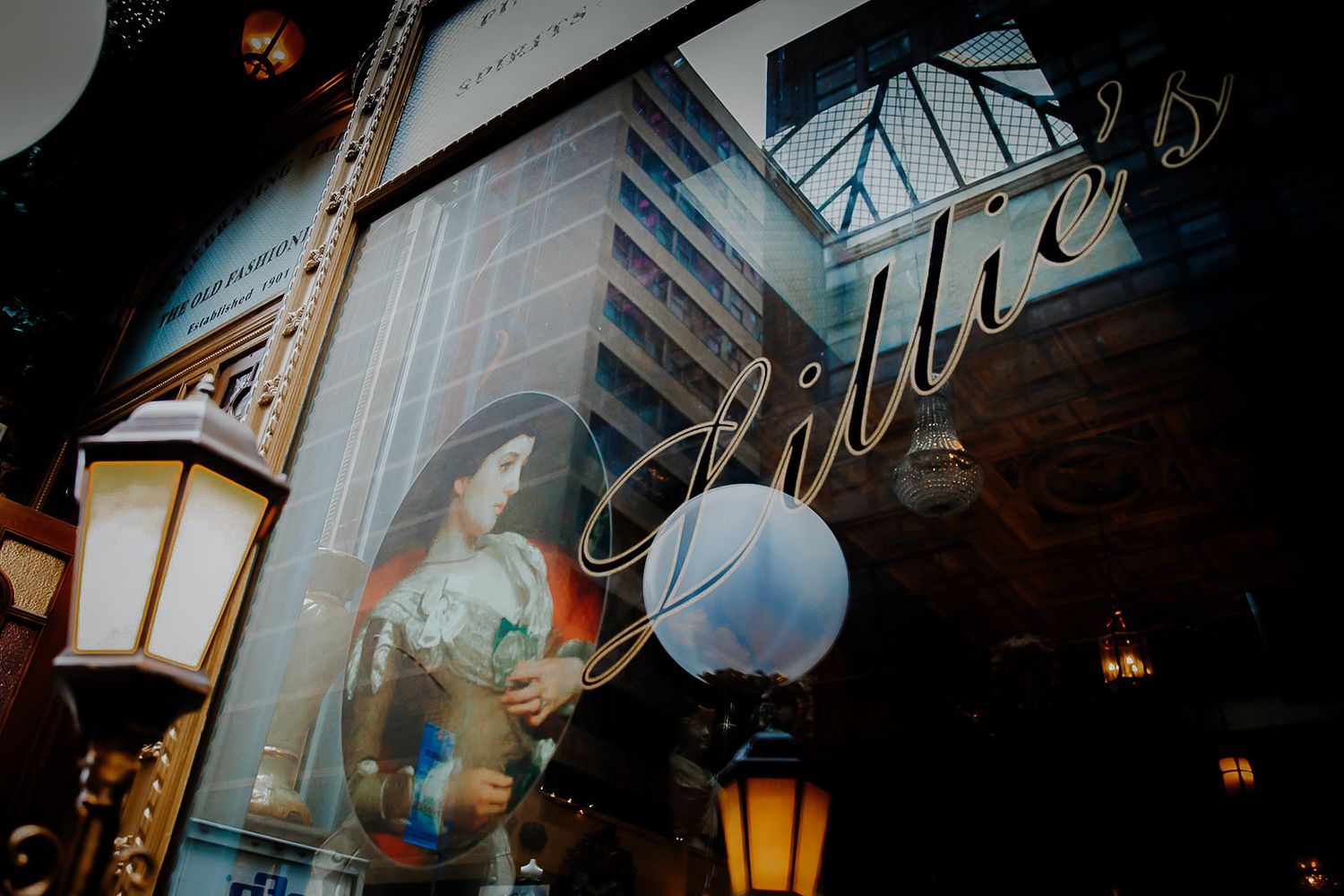Vintage lantern lights mounted on dark wooden posts illuminate a covered walkway with glass ceilings at night.