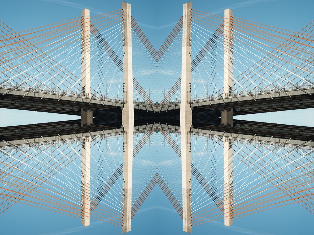 Panoramic view of a modern cable-stayed bridge with white towers reflecting in calm water against a blue sky.
