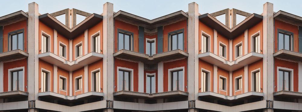 Modern apartment building with orange facade and geometric angular balconies creating a zigzag pattern across the exterior.