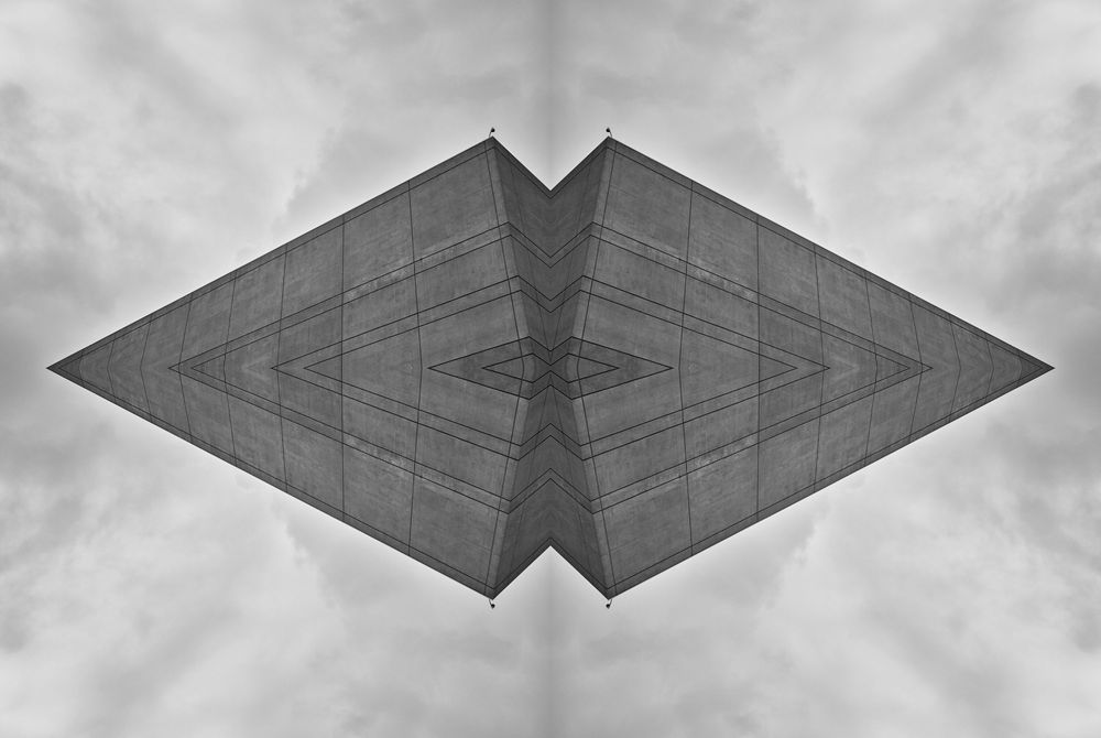 Abstract architectural detail of a diamond-shaped structure against cloudy sky in black and white.