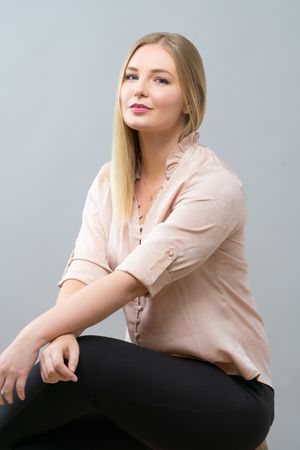 Professional portrait of person in light pink blouse and dark pants against gray background looking upward.
