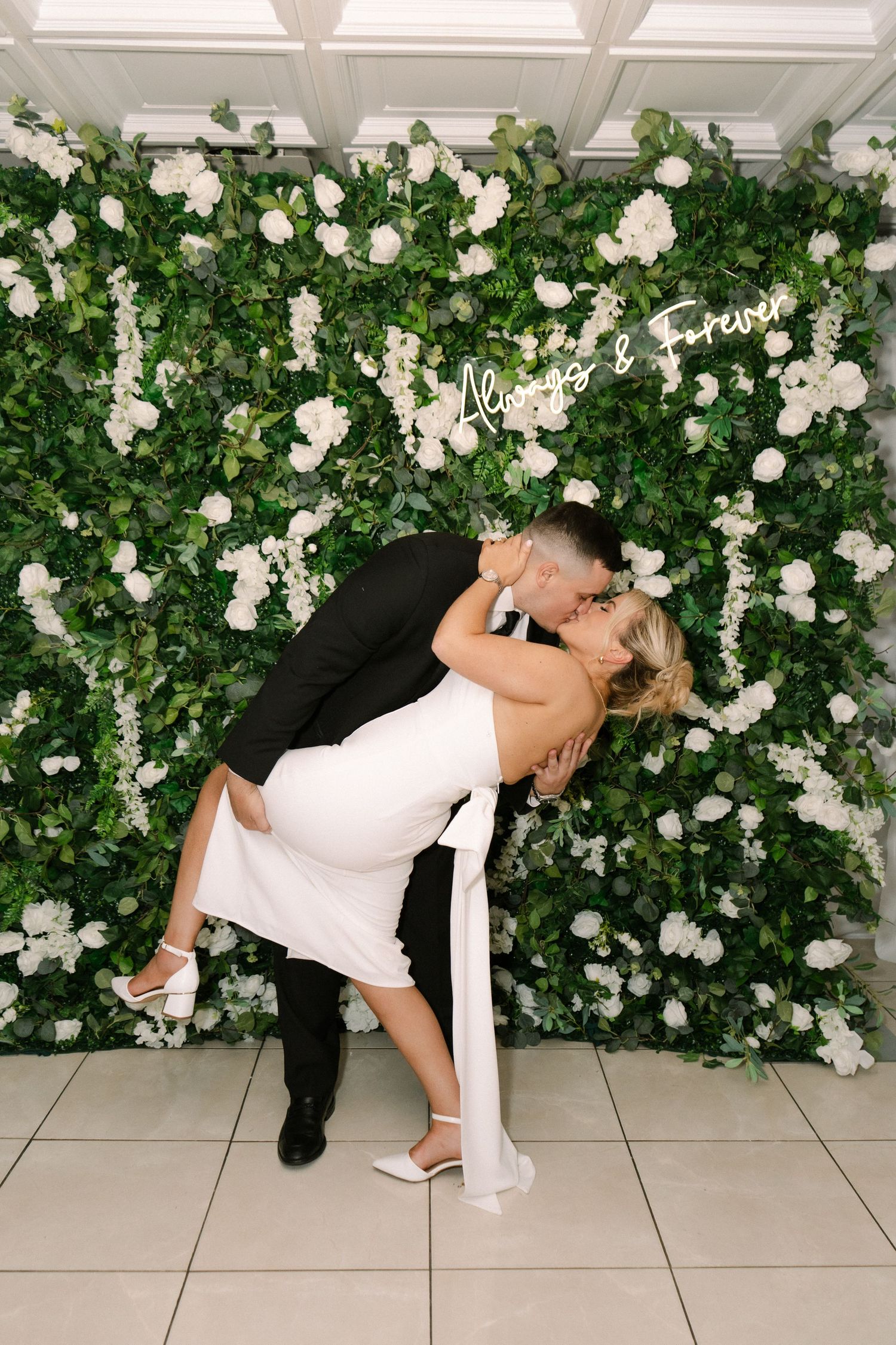A couple shares a playful dance moment outdoors in a park setting with green trees in the background.