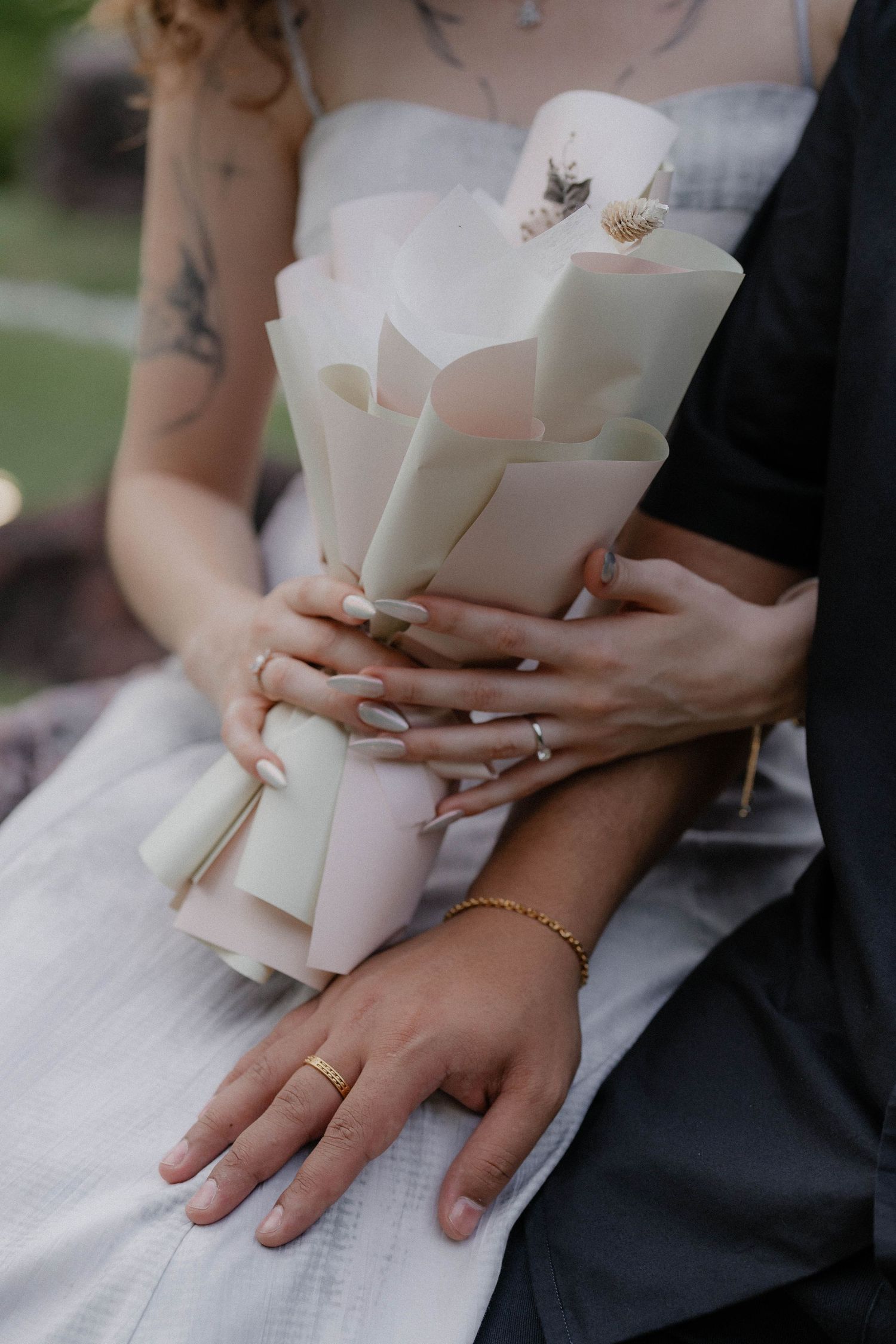 A close-up shot of hands holding an elegant white paper bouquet with matching rings.