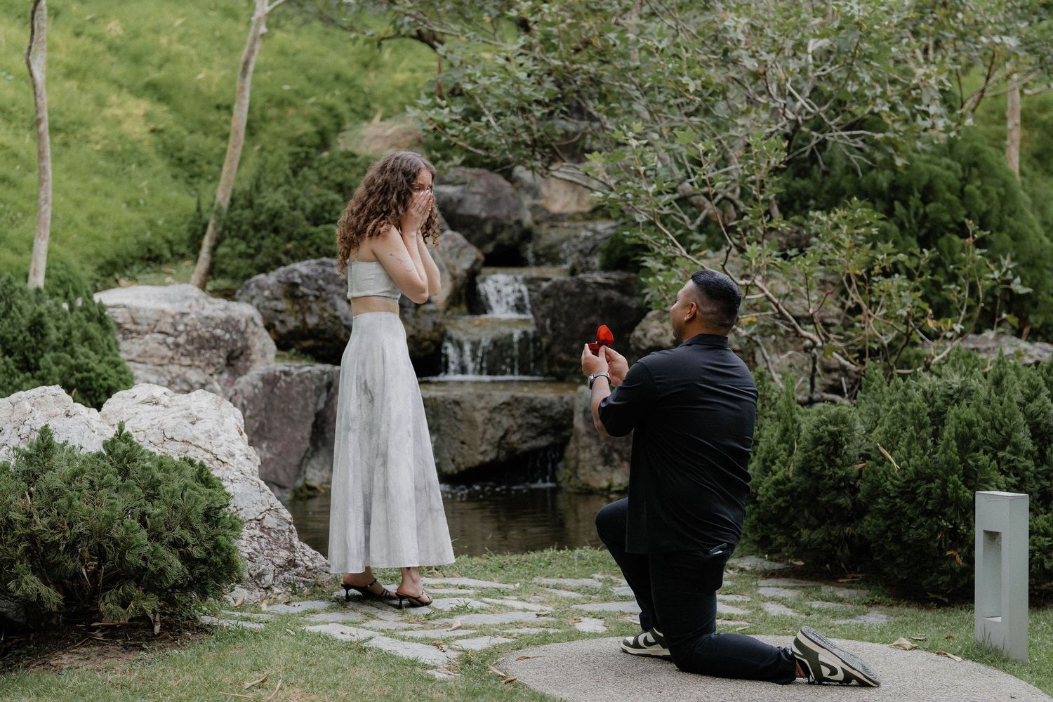 A romantic wedding photo session taking place among rocks and trees in a garden setting.