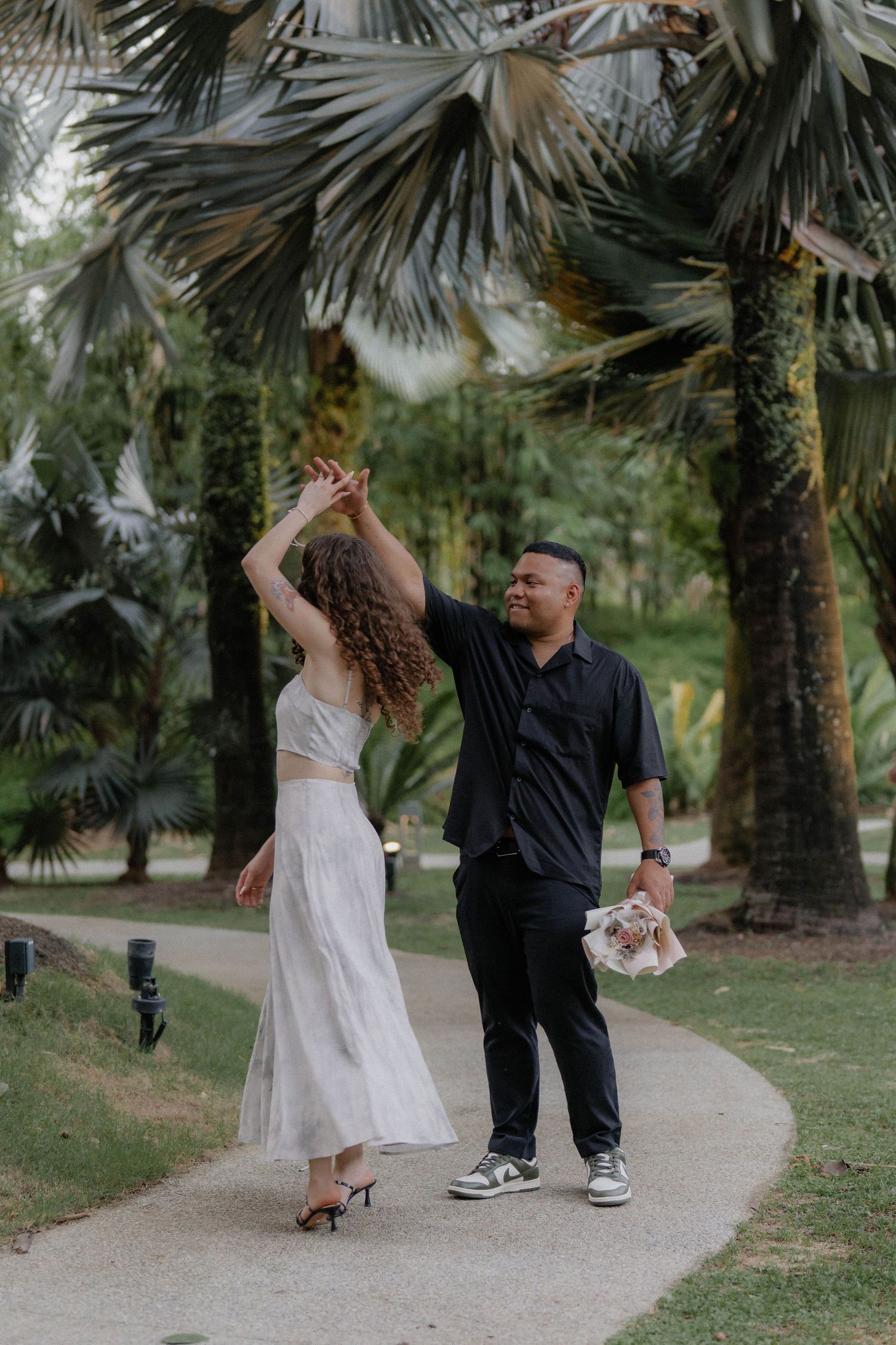 A romantic couple walking along a palm-lined pathway in their wedding attire during a photo session.