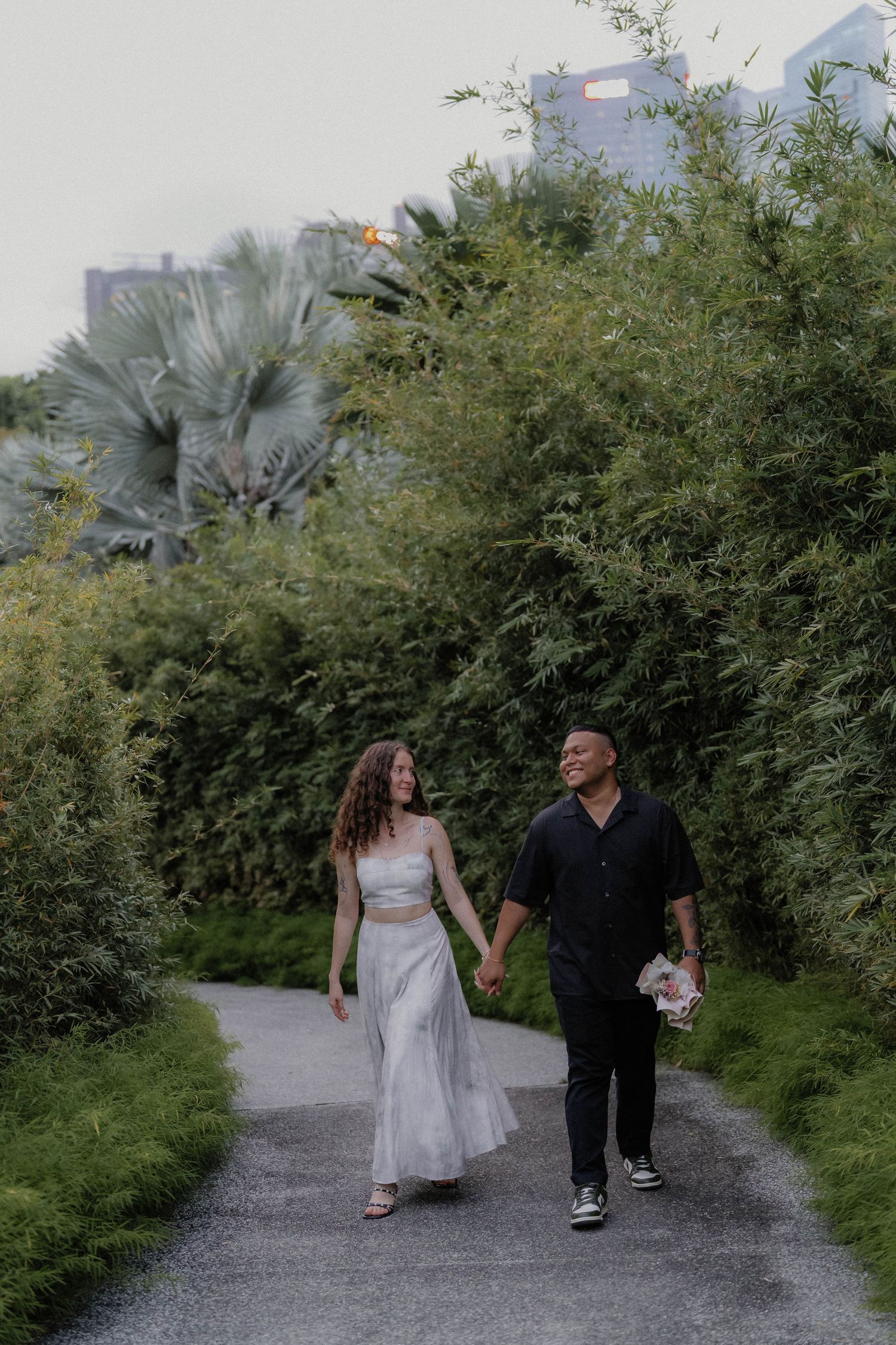 A couple strolling down a scenic garden path surrounded by lush greenery and palm trees.