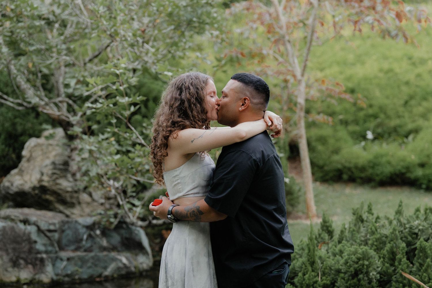A tender embrace shared in a lush garden setting with rocks and greenery.