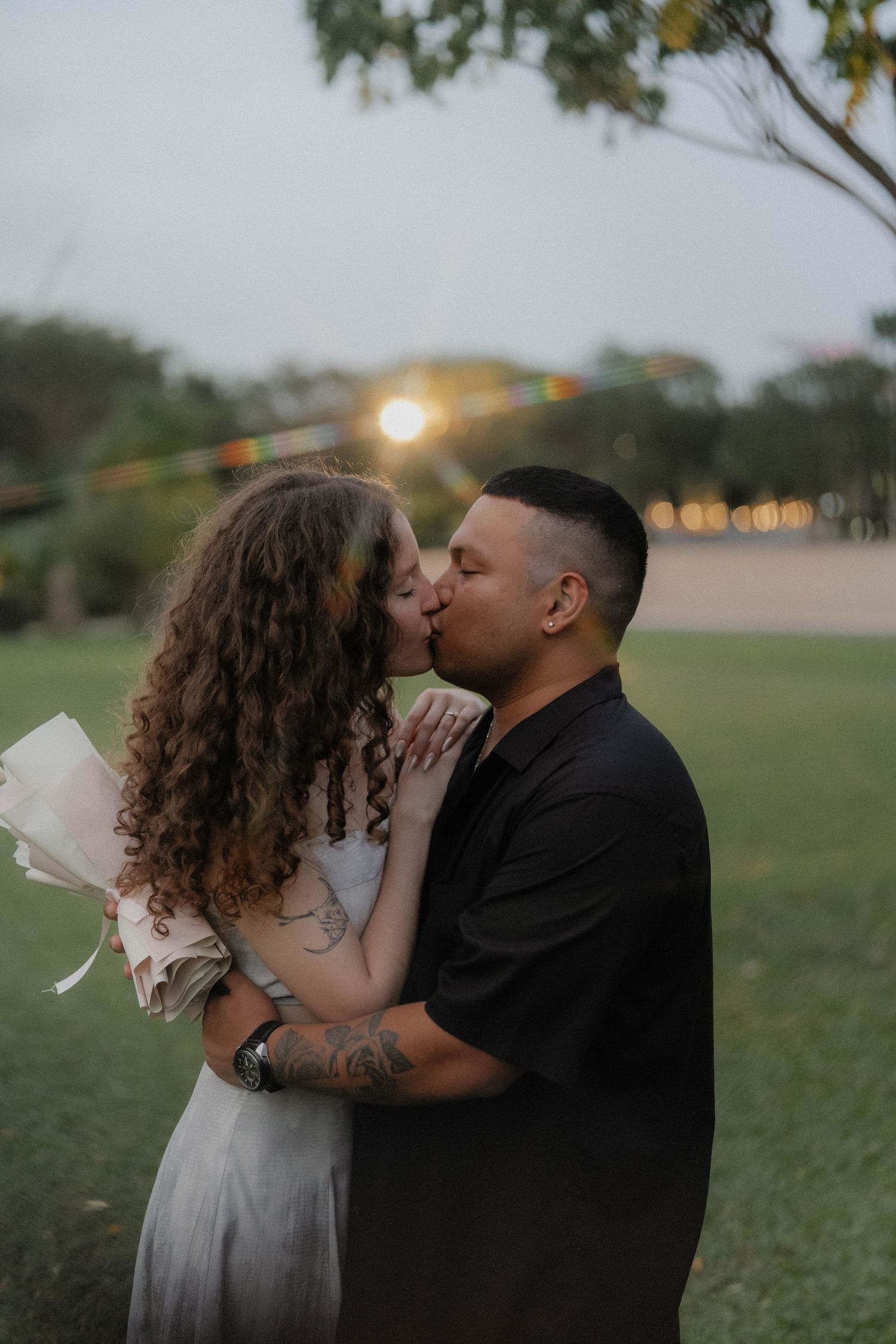 A romantic kiss in a park at sunset with soft lighting.
