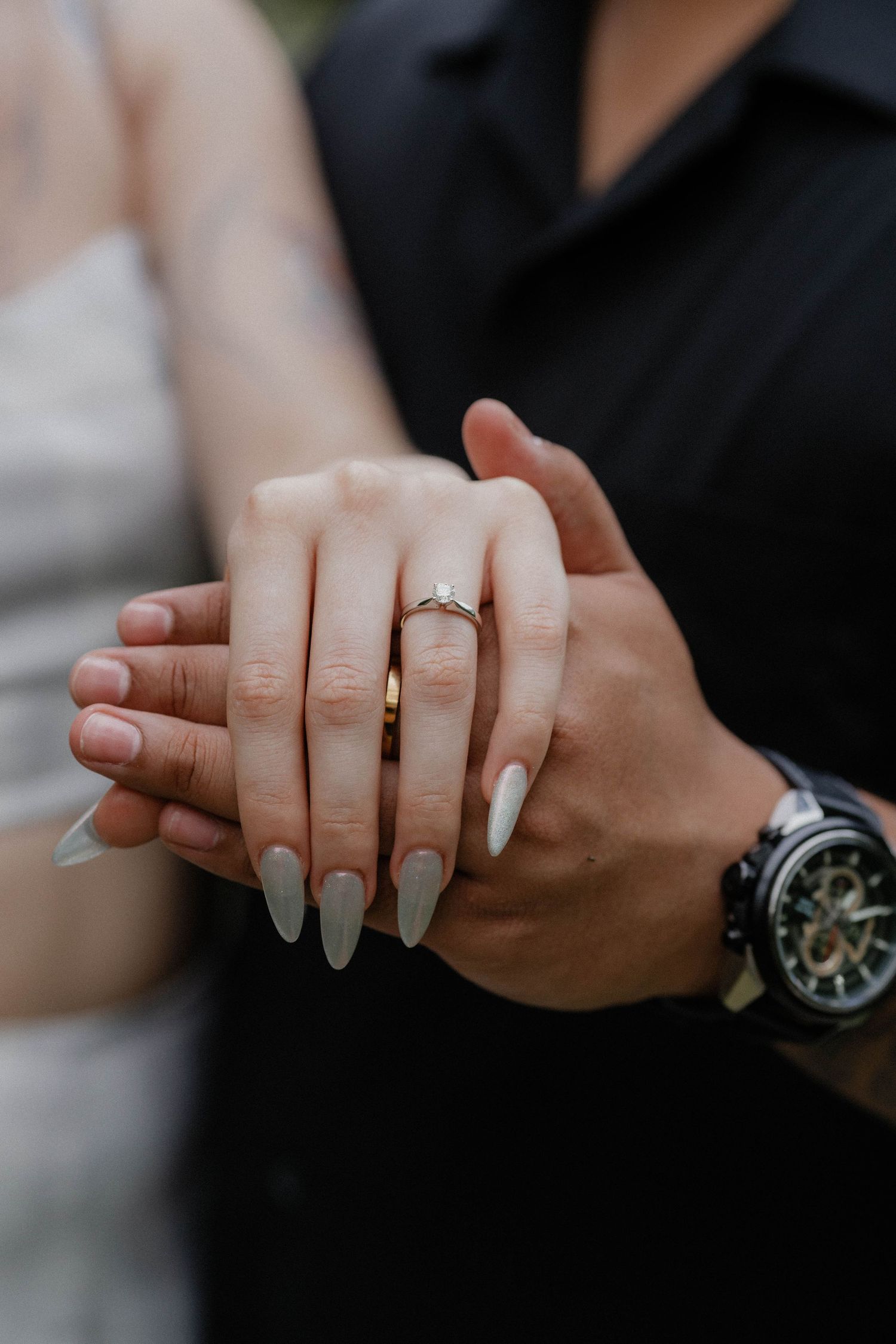 Close-up of hands showing an engagement ring, with one person wearing a black watch.